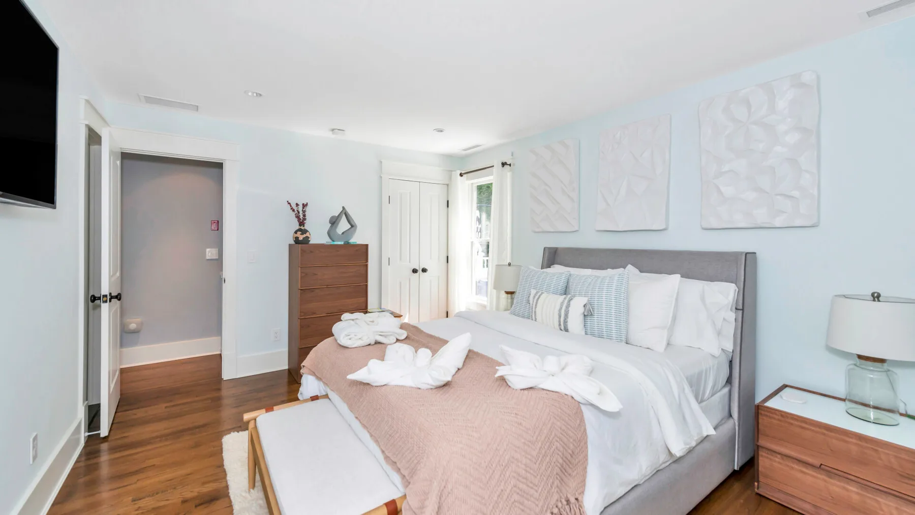 A bright bedroom with a large bed and pale wall decor.