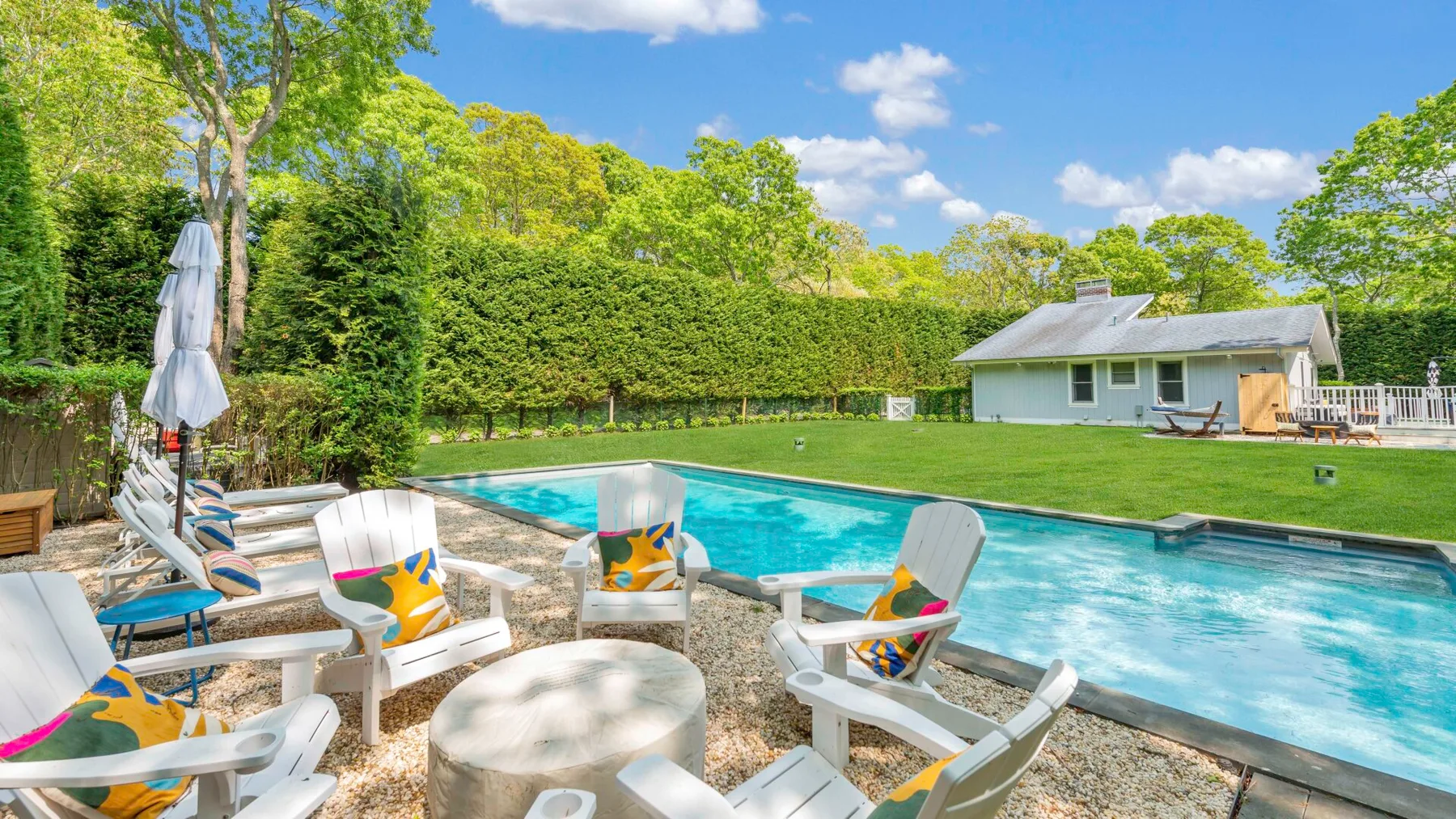 An outdoor swimming pool is surrounded by lounge seating and a green lawn.
