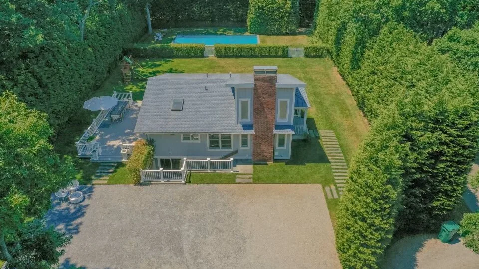 An aerial view of a house, driveway, surrounding trees, and a swimming pool.
