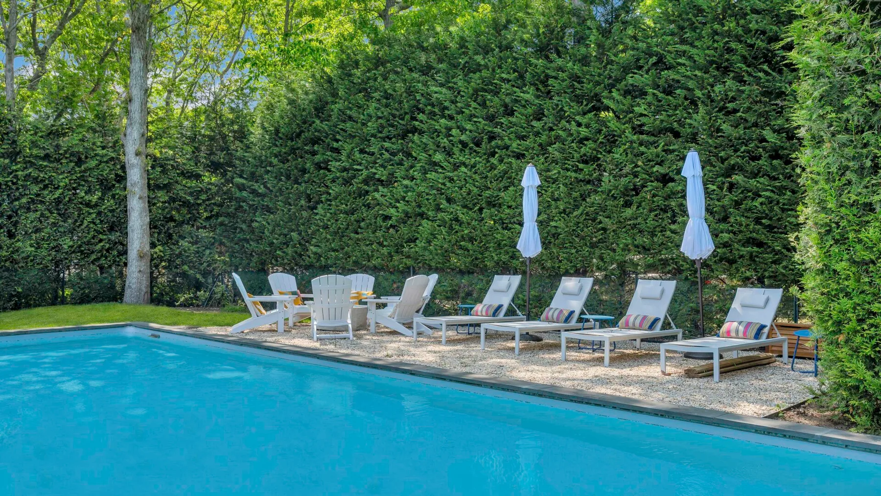 An outdoor swimming pool sits beside loungers and closed umbrellas.