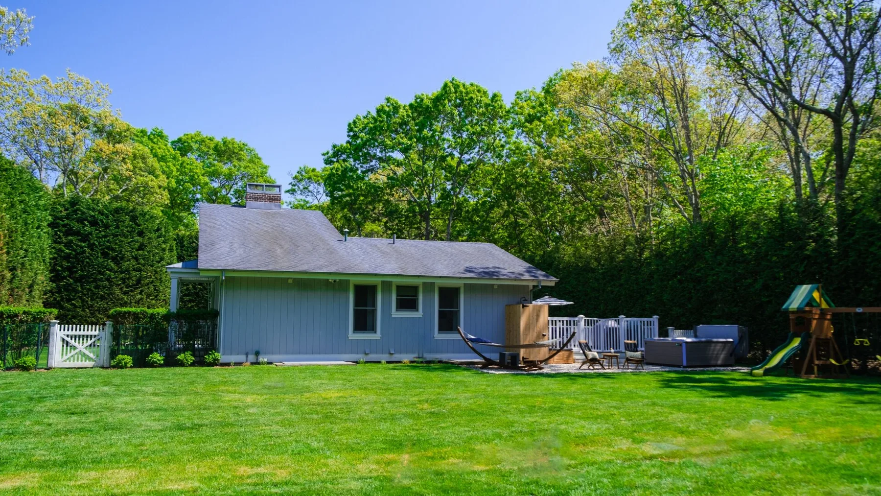 A house with a wide green lawn and a fenced patio surrounded by trees.