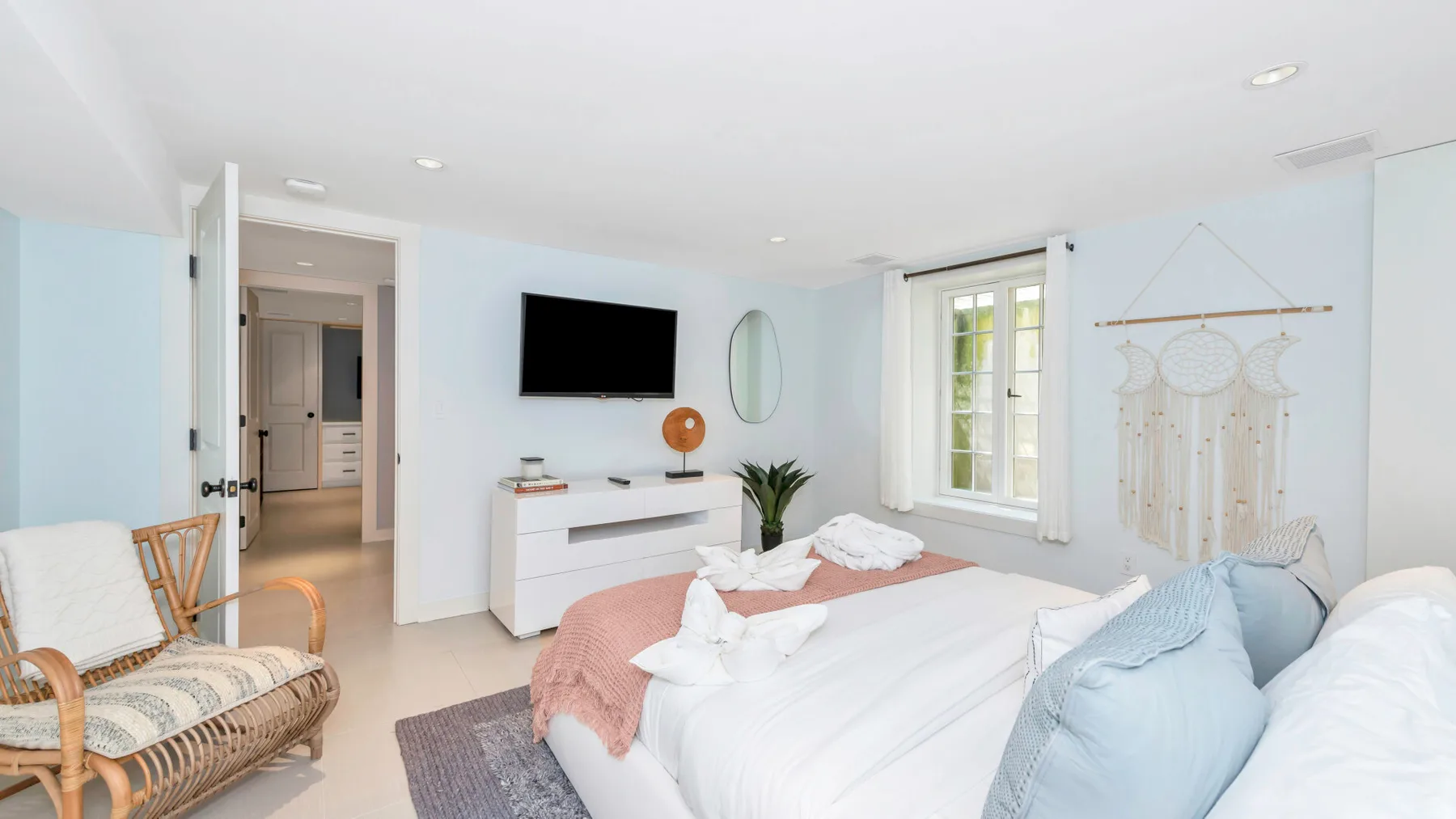 A bright bedroom with a bed, a television, and a wicker seating area.