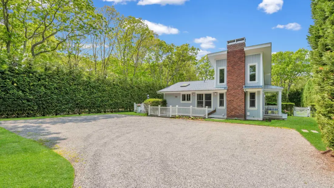 A modern house with a brick chimney stands beside a broad gravel driveway.