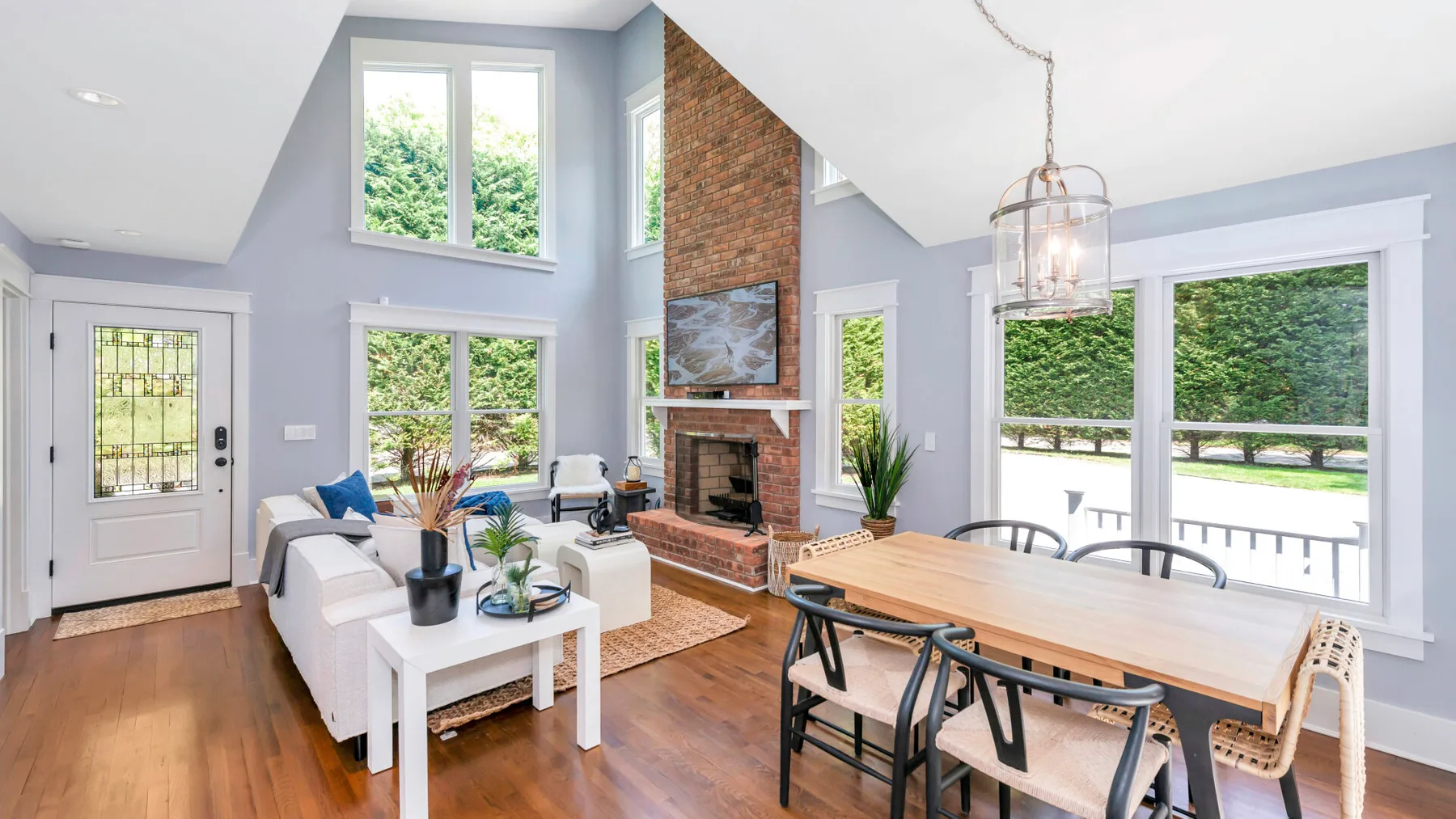 A bright living and dining room with a brick fireplace and large windows.