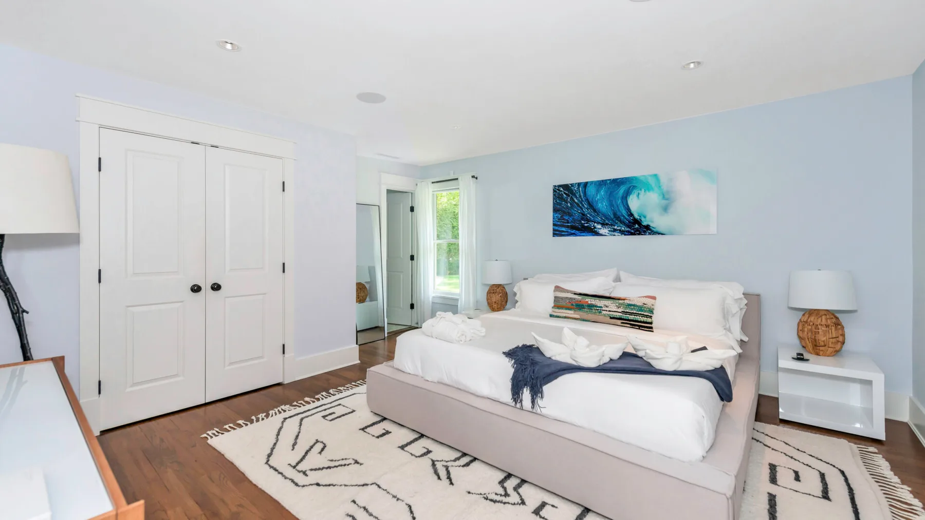 A bright bedroom with a bed, wall-mounted artwork, and a patterned rug.