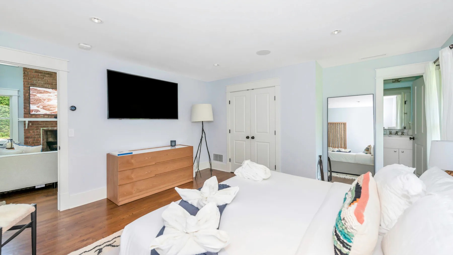 A bright bedroom with a large bed, wooden dresser, and wall-mounted television.