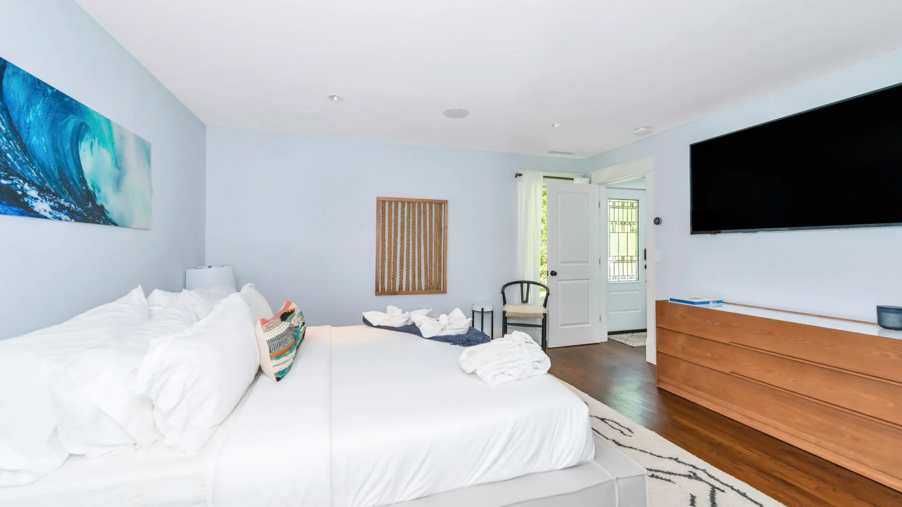 A bright bedroom with white bedding, colorful wall art, and a television.