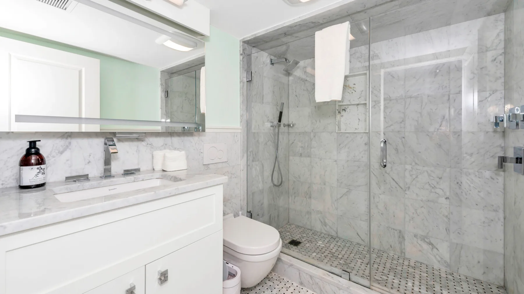 A bright bathroom with a white vanity, toilet, and glass-enclosed shower.
