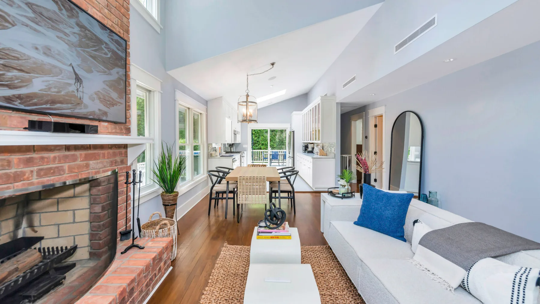 A bright living room with a brick fireplace, dining area, and white seating.