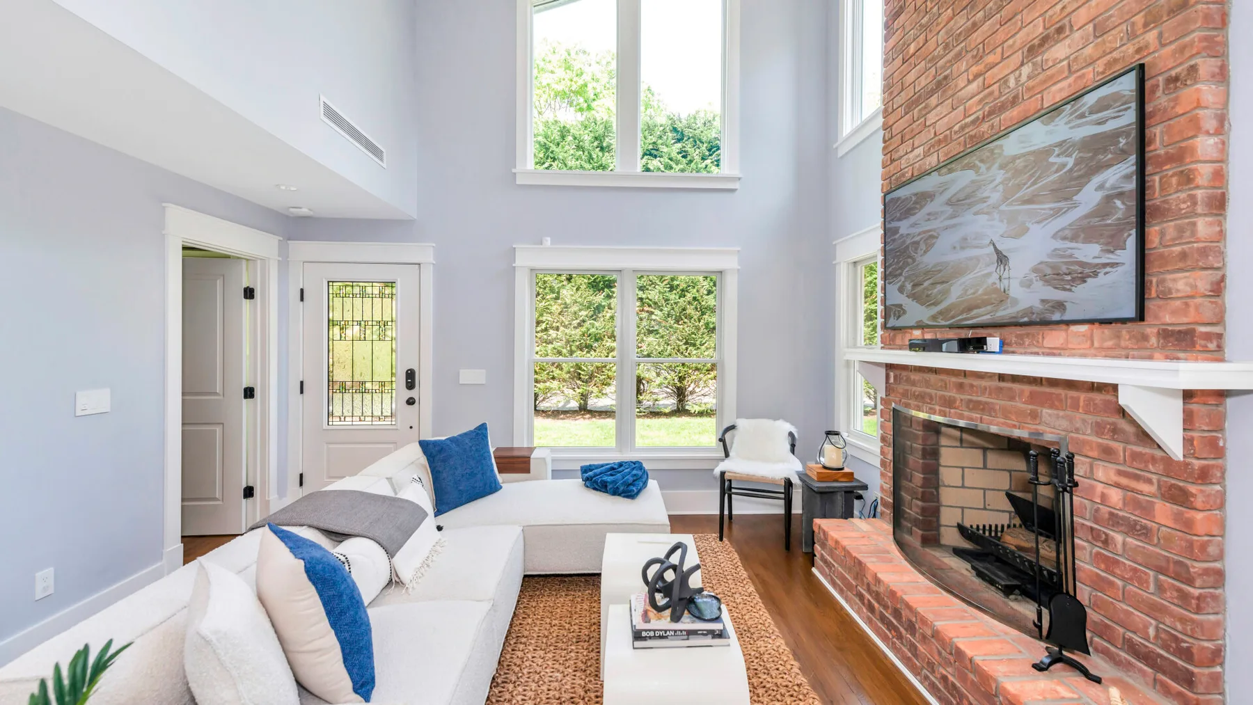 A bright living room with seating, tall windows, and a brick fireplace.
