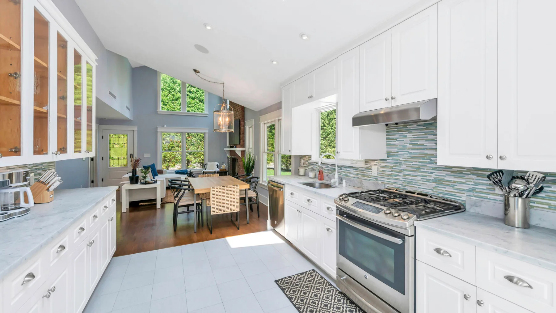 A bright kitchen with white cabinetry, a cooking range, and a dining table by the windows.