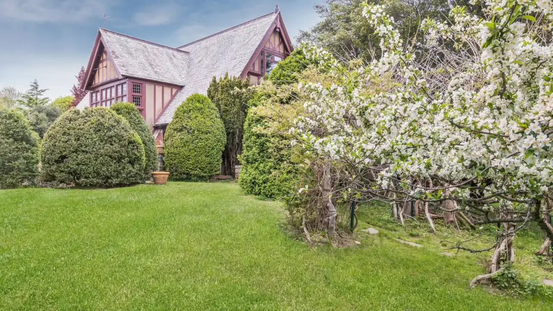 Un jardín con césped verde, arbustos en flor y una casa de madera.