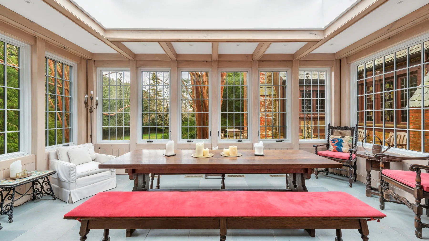 Un solárium luminoso con una mesa larga de madera y un banco tapizado en rojo.
