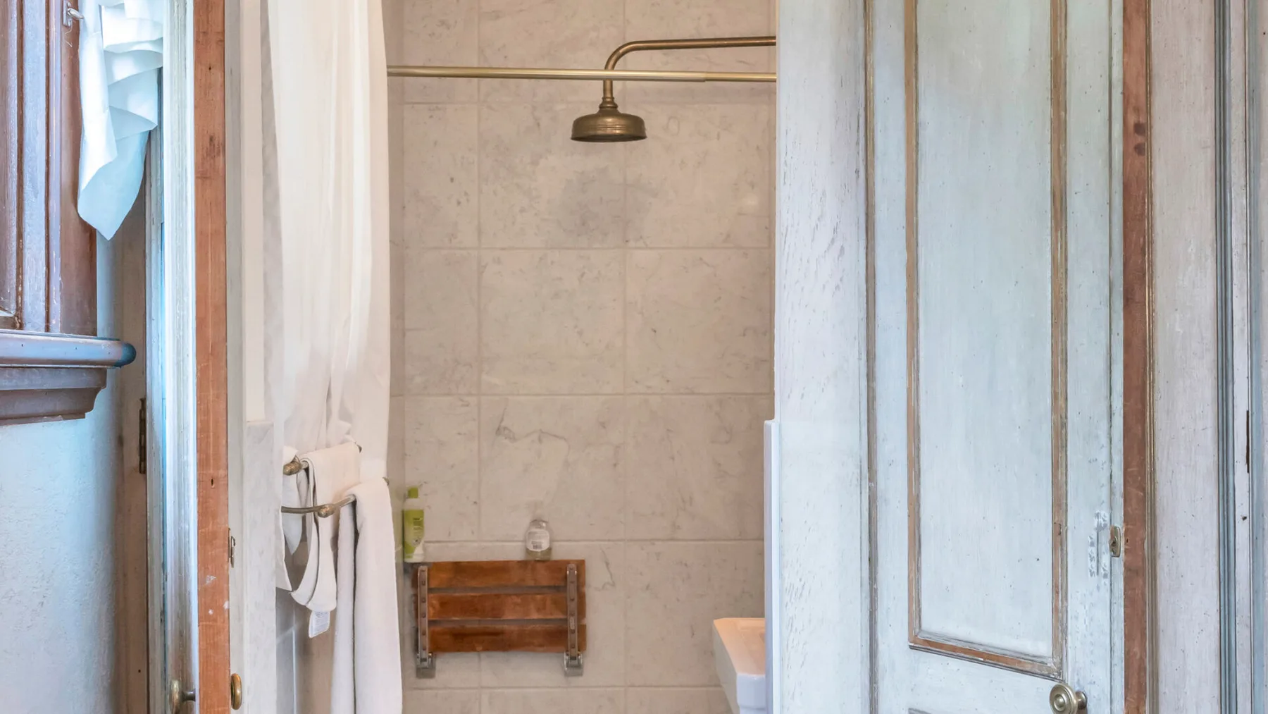 Un baño con azulejos, una ducha y un estante de madera en la pared.