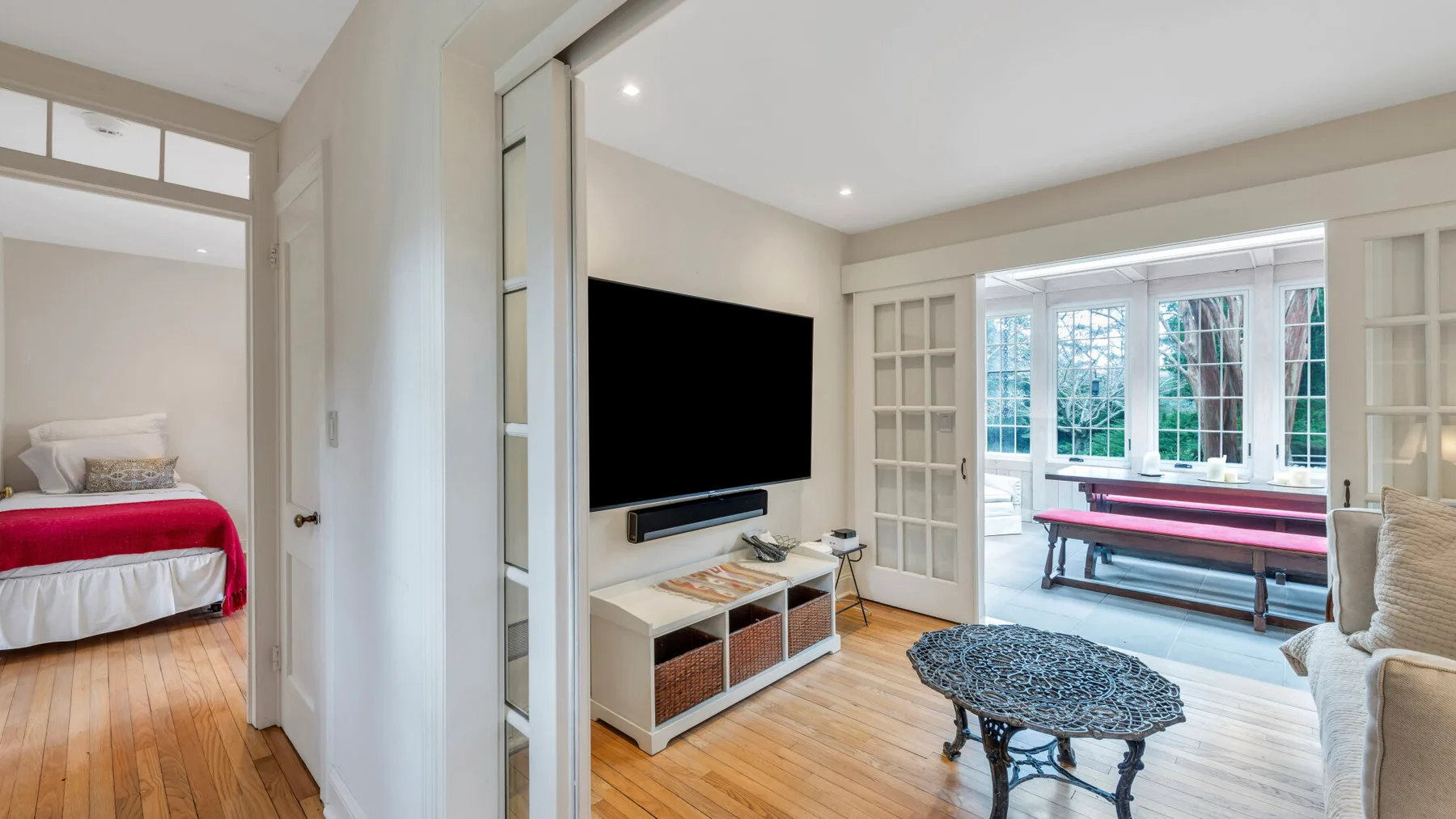 Una sala luminosa con televisor, asientos y ventanas grandes.