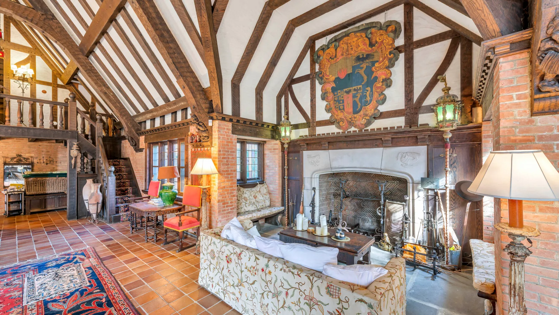 Una sala de estar con vigas de madera, una gran chimenea y asientos estampados.