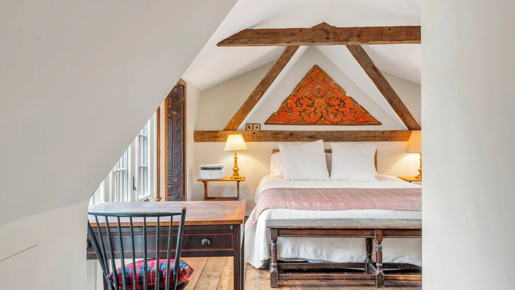 Un dormitorio con una cama bajo vigas de madera vistas y un adorno triangular en la pared.