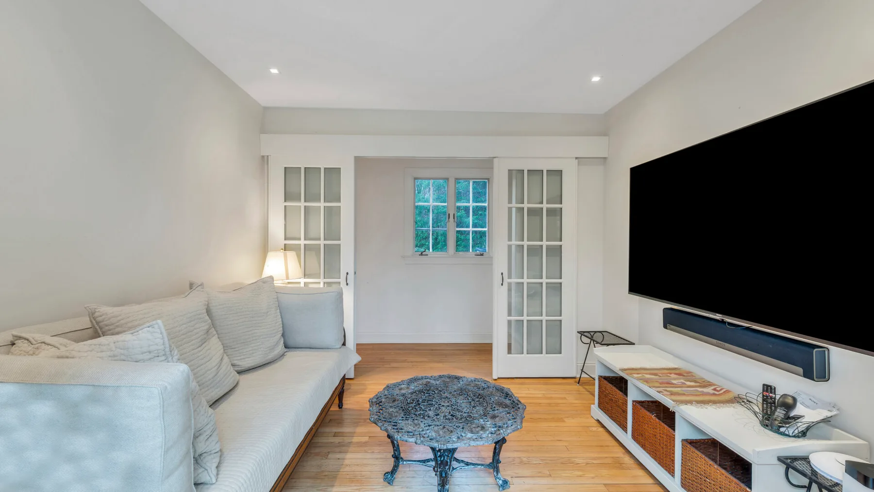 Una sala luminosa con un sofá largo, una mesa de centro y un televisor montado en la pared.
