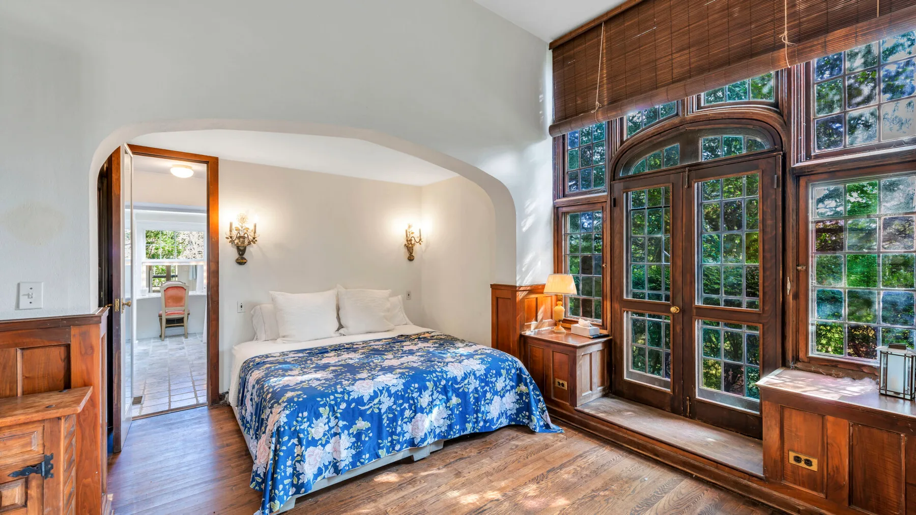 Un dormitorio con una cama bajo un arco, junto a ventanas altas.