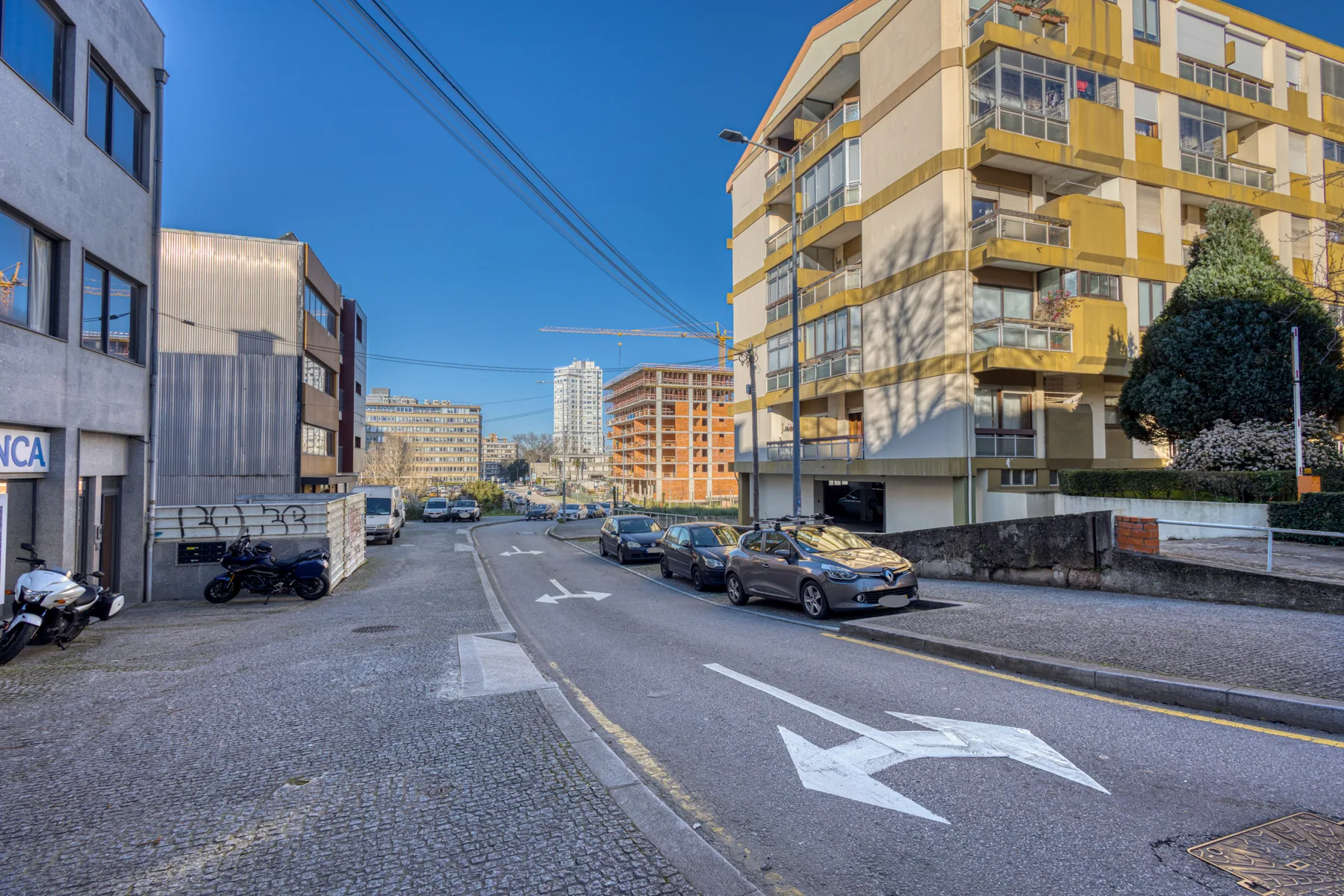 A city street with parked cars and buildings beneath a clear blue sky.