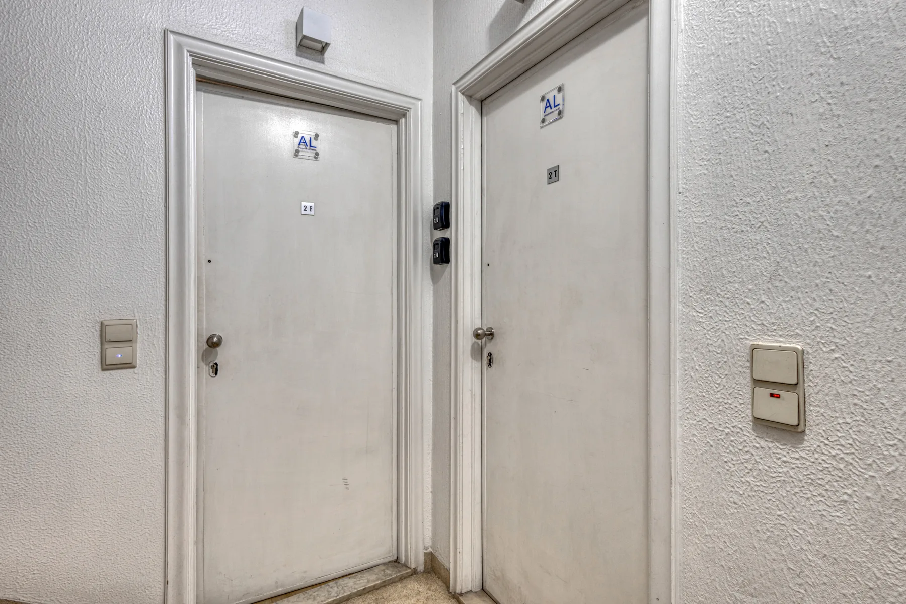 An indoor hallway with two light-colored doors and wall switches.