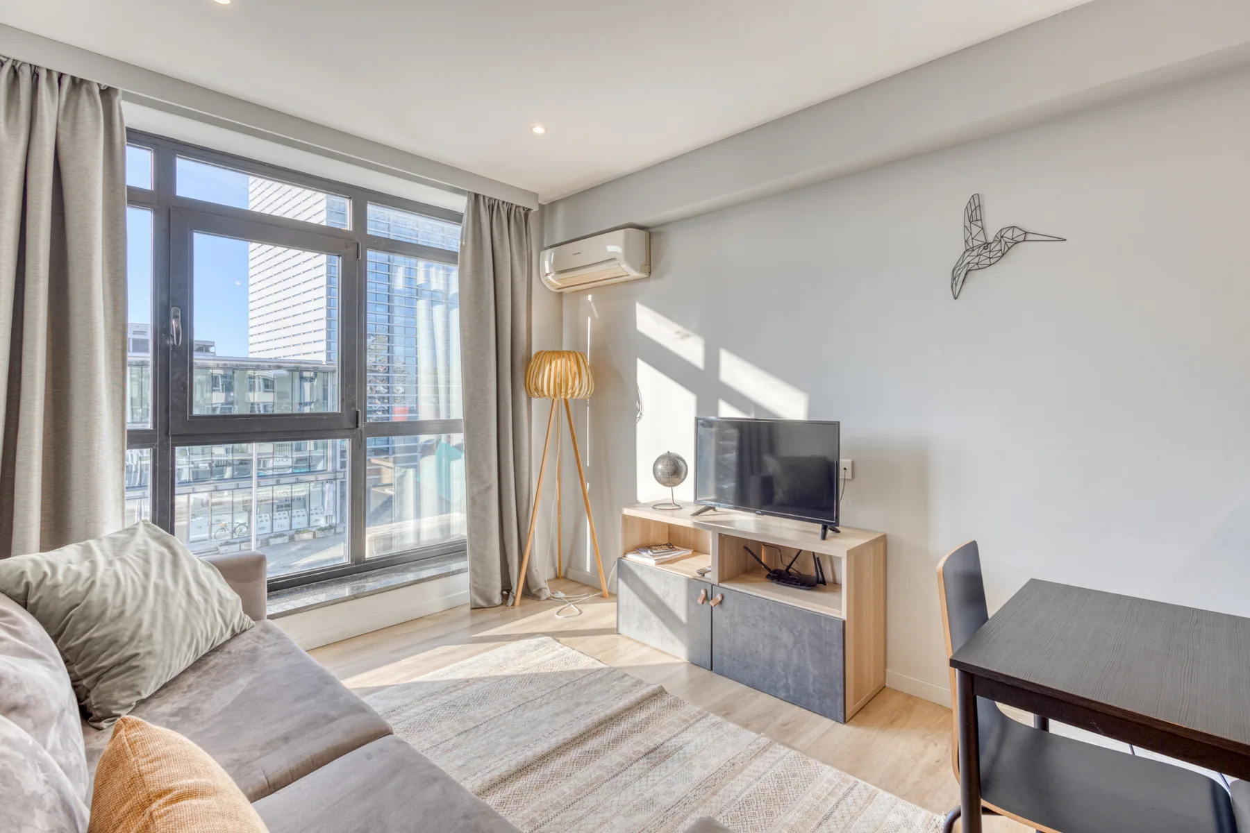 A bright living room with seating, a television, and large windows.