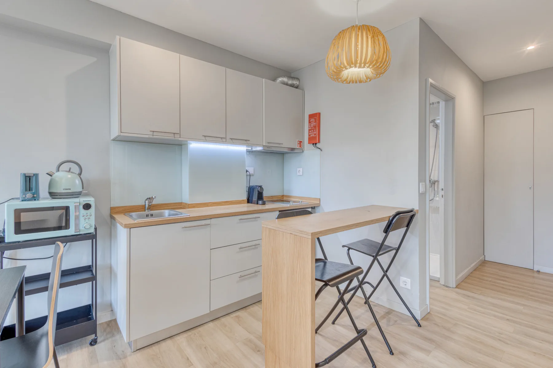 A compact kitchen and dining area with pale cabinetry, a counter, and folding chairs.