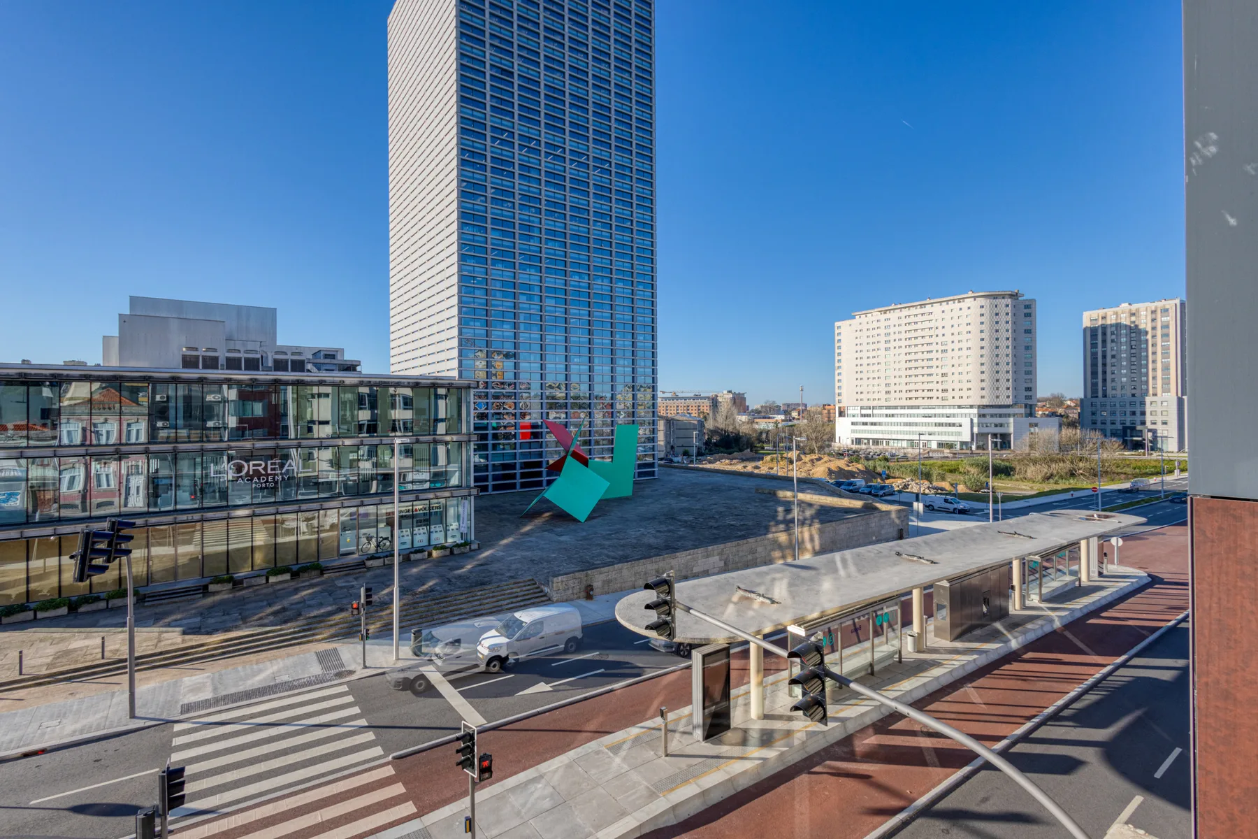 An urban cityscape with a tall glass tower and a tram stop in the foreground.