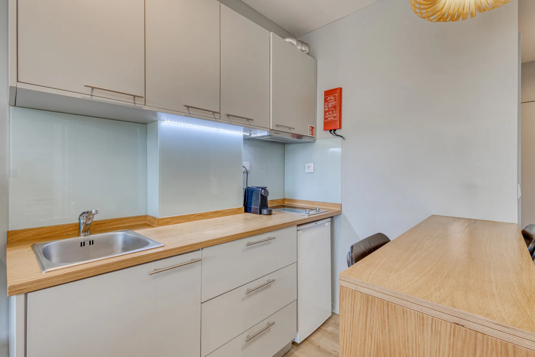 A compact kitchen with light cabinetry, a sink, and a wooden countertop.