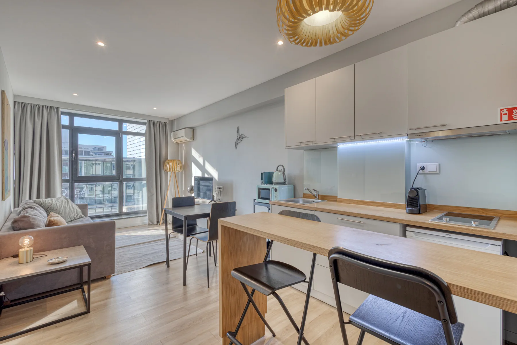 An open-plan apartment interior with a kitchen island and dining area beside large windows.