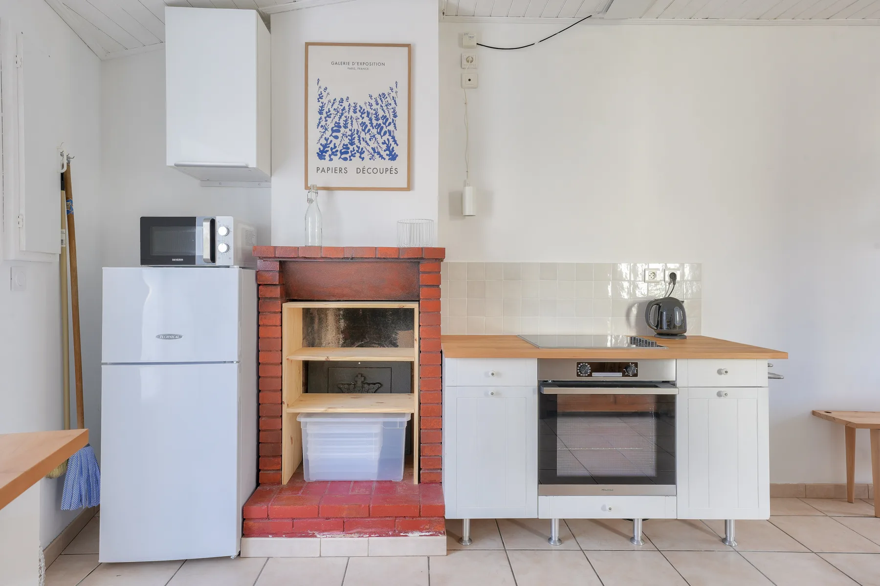 A compact kitchen with white cabinets, an oven, and a brick fireplace.