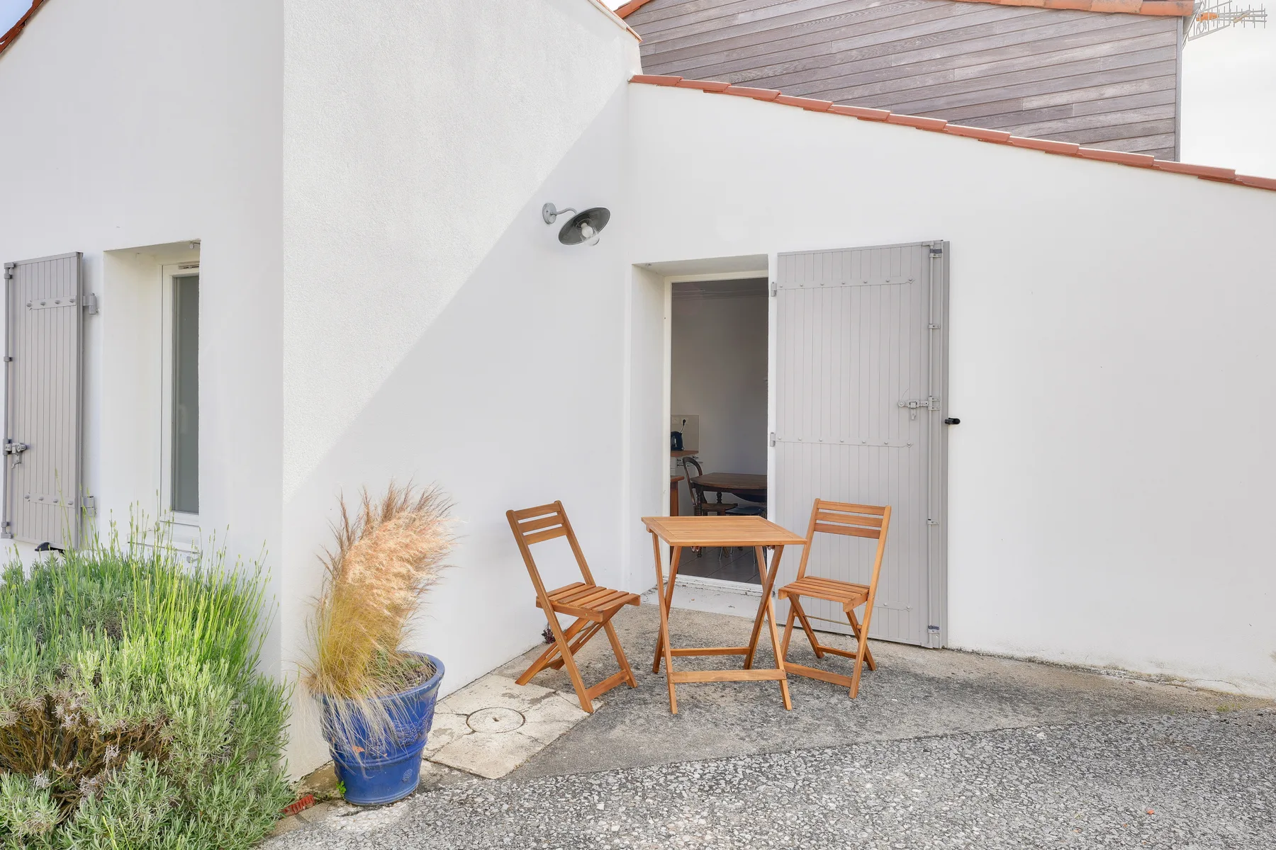 An outdoor patio has a wooden table and chairs beside an open doorway.