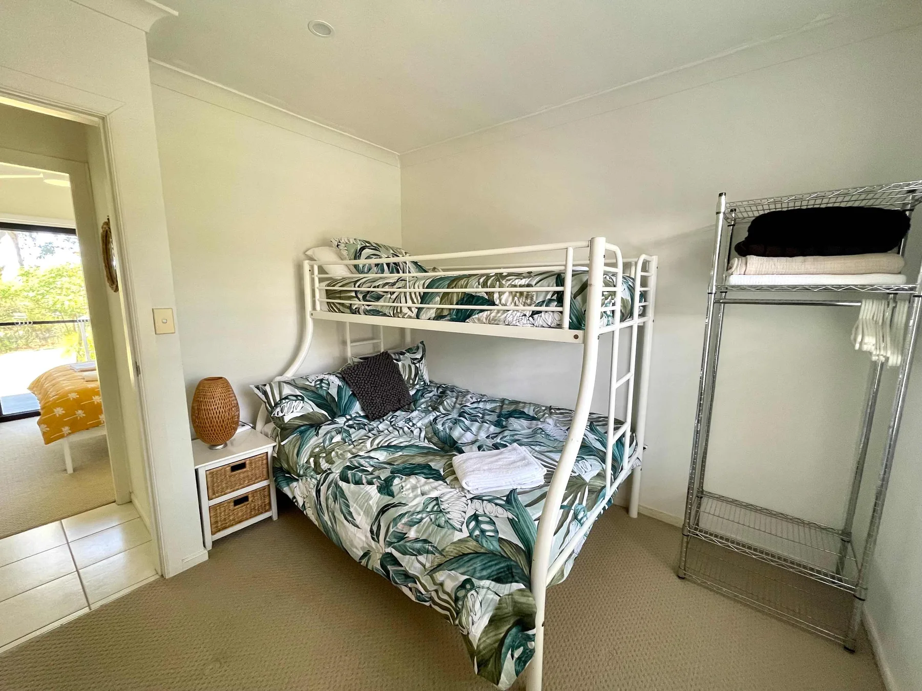 A bedroom with a bunk bed, patterned bedding, and a metal clothes rack.