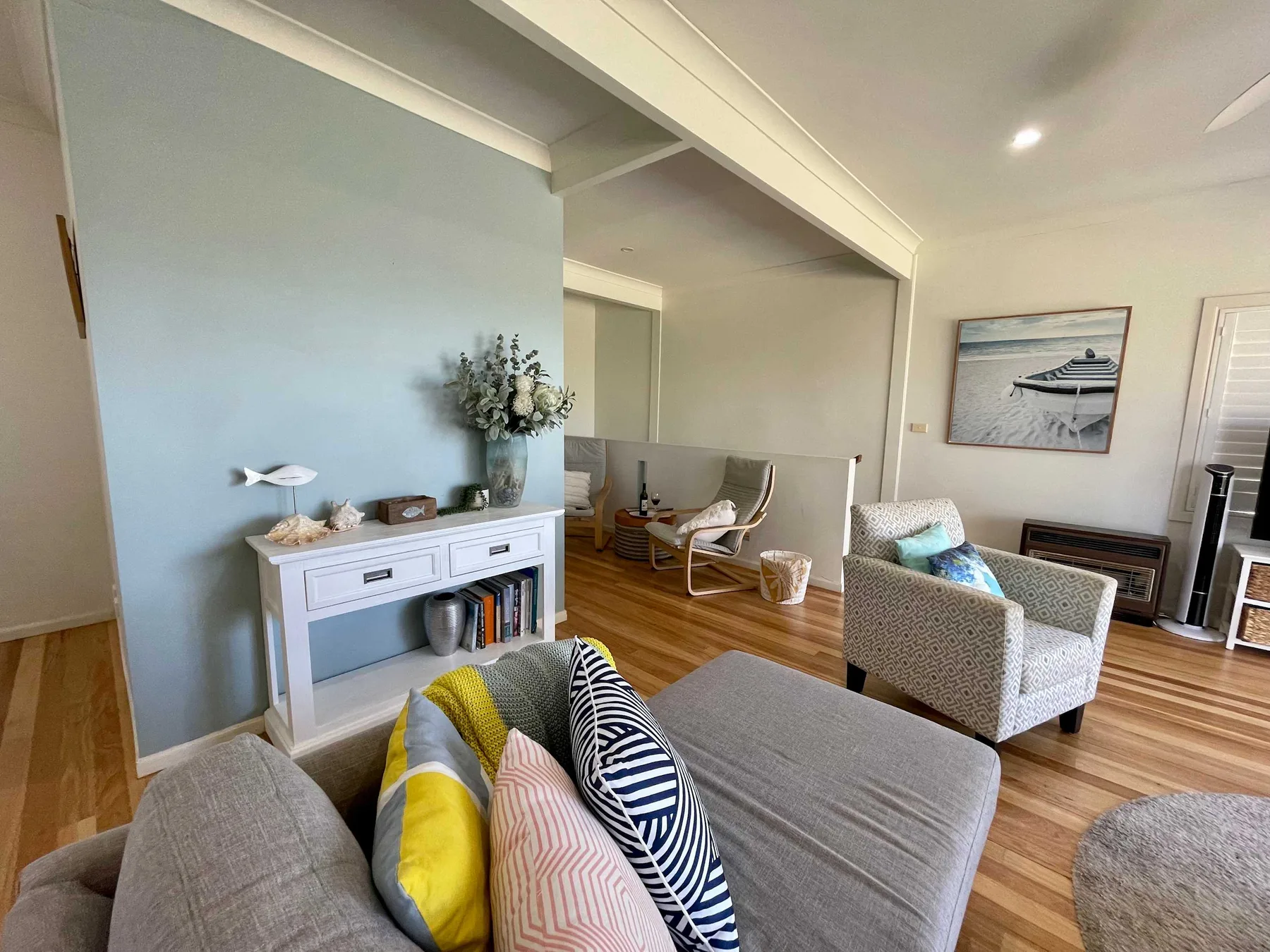 A bright living room with seating, a fireplace, and framed coastal artwork.