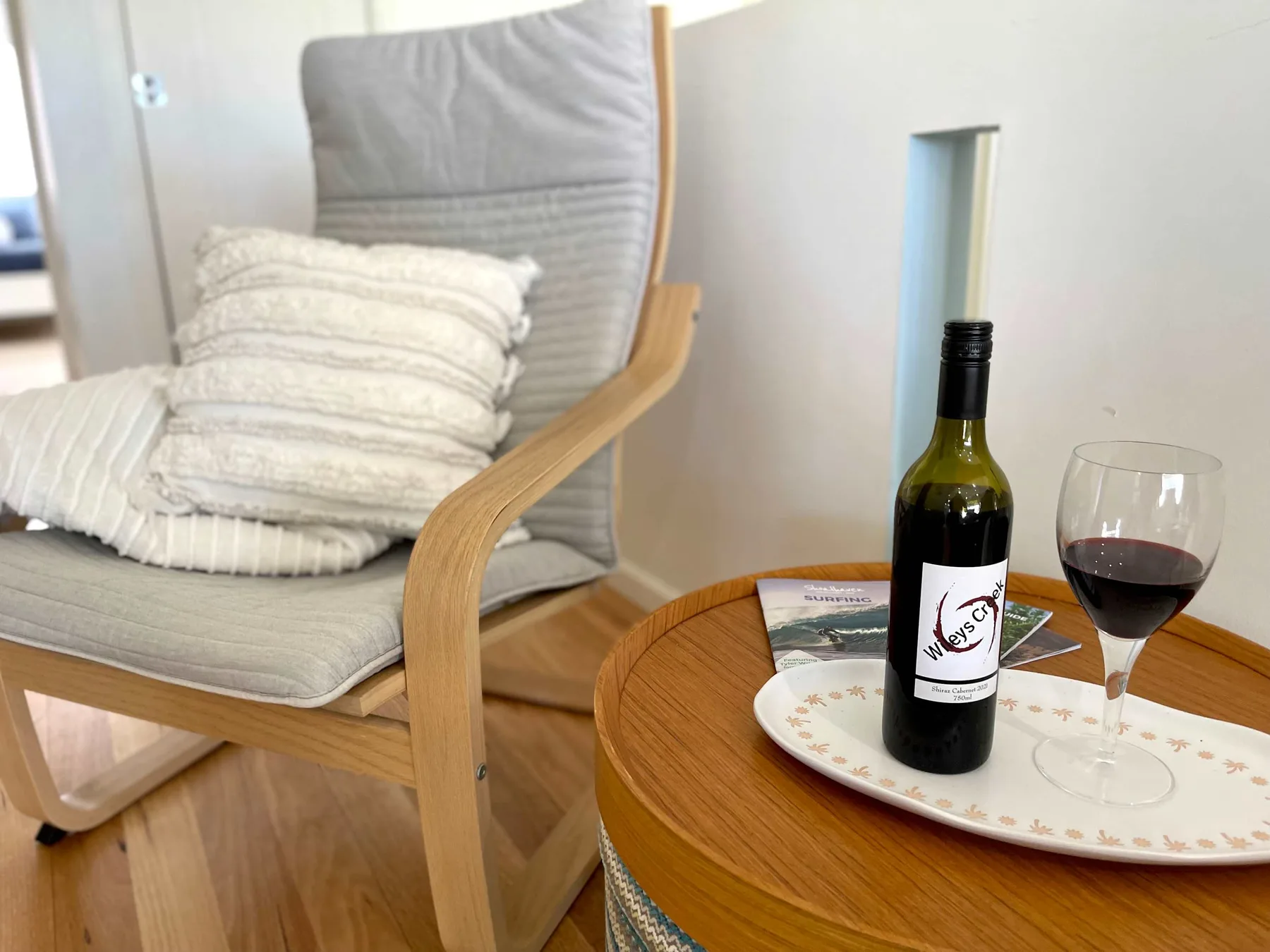 A seating area with a cushioned chair and a round table holding wine.