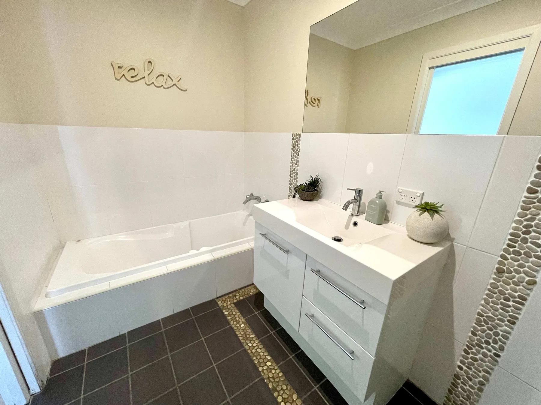 A bathroom with a bathtub, white vanity, and pebble-tile accents.