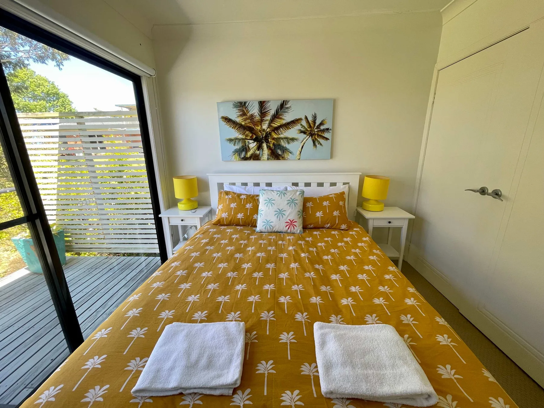 A bedroom with a bed dressed in a palm-tree print and a sliding glass door.