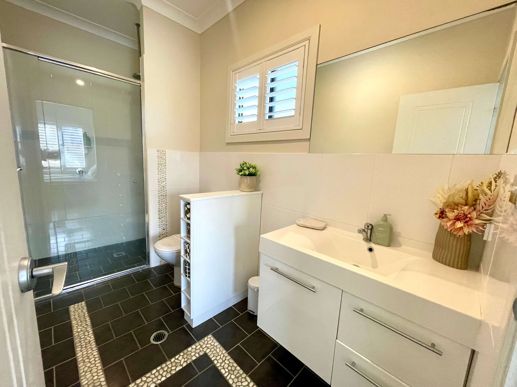 A bright bathroom with a glass shower and a long sink vanity.