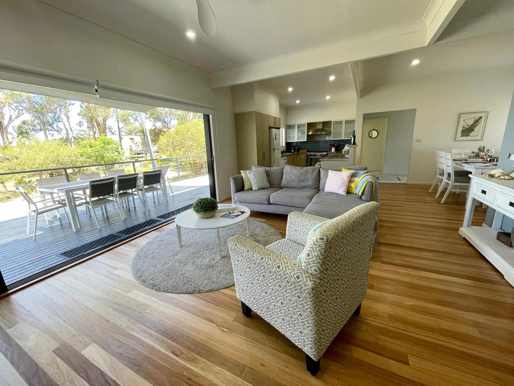 A bright living room opens onto a balcony, with seating and a dining area.