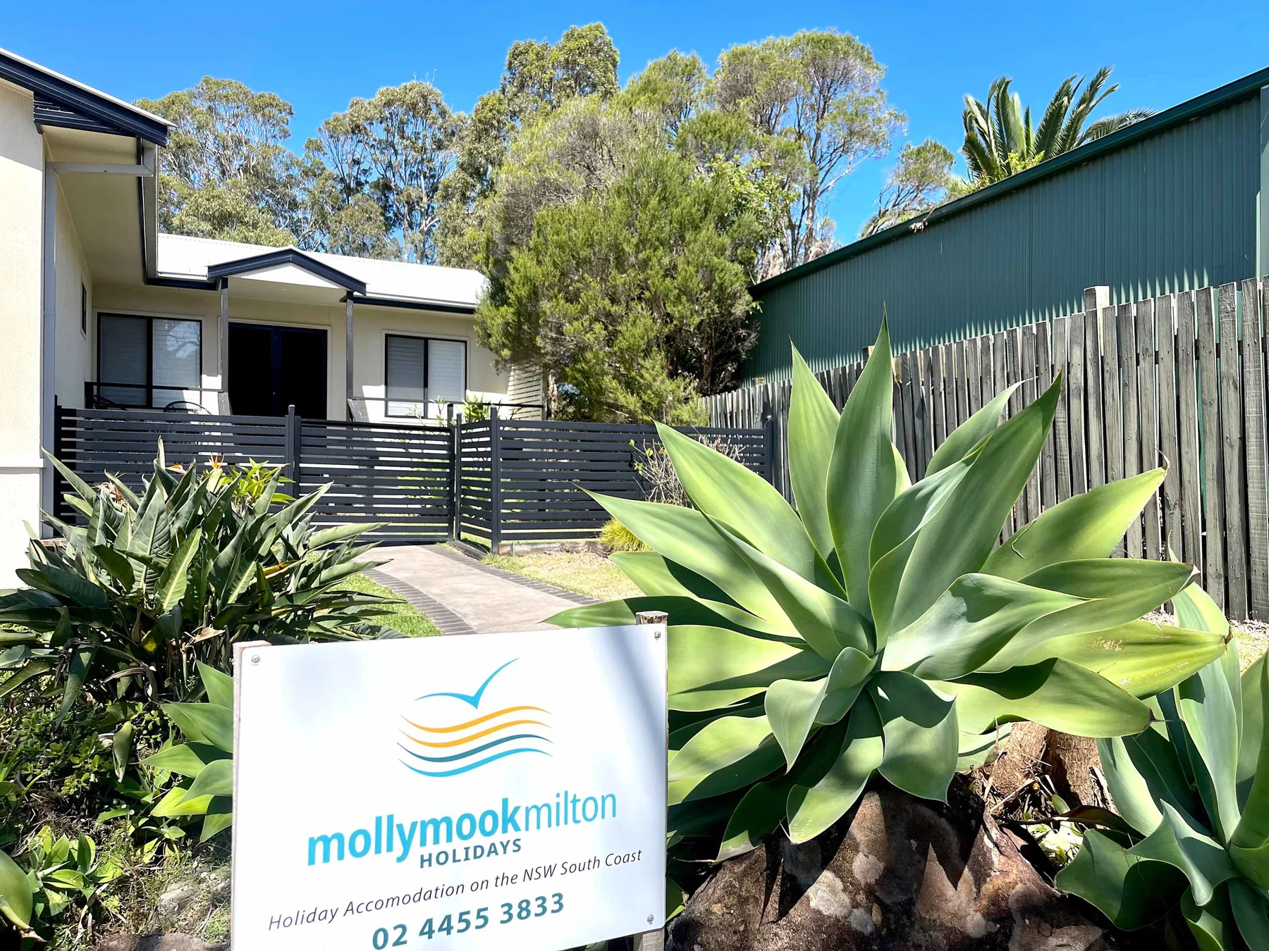 A holiday property entrance with a sign and leafy plants.