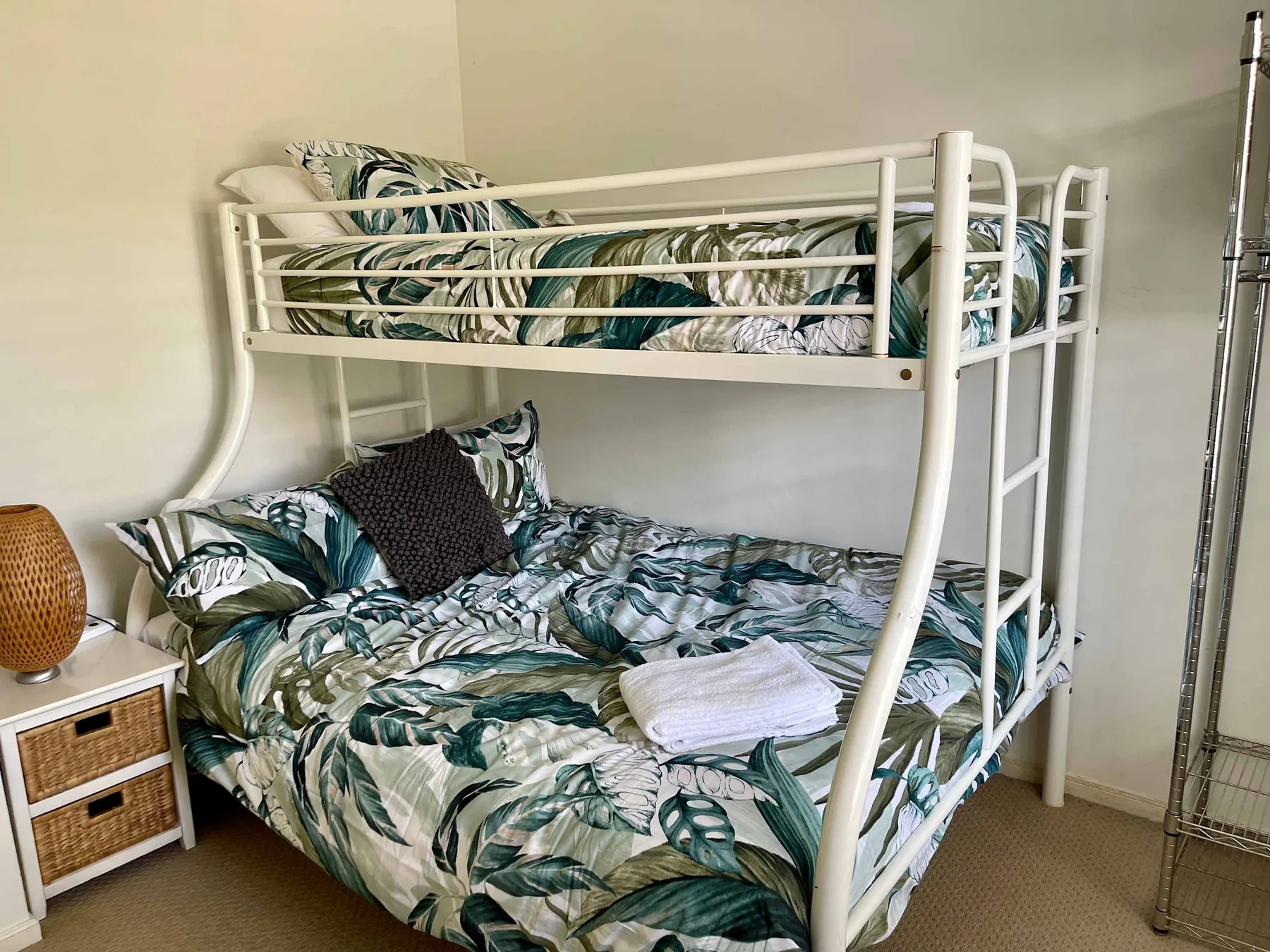 A bunk bed with green leaf-patterned bedding stands against a light wall.
