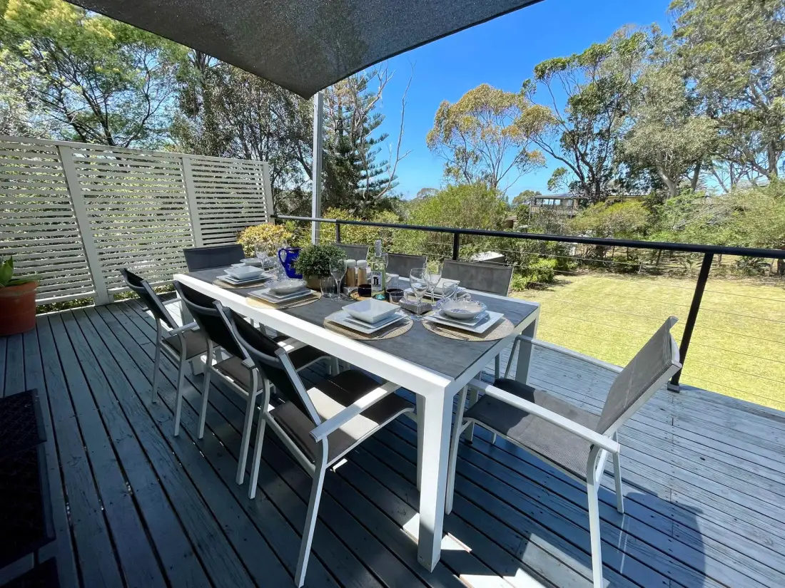 An outdoor dining area on a deck overlooks a grassy yard and trees.