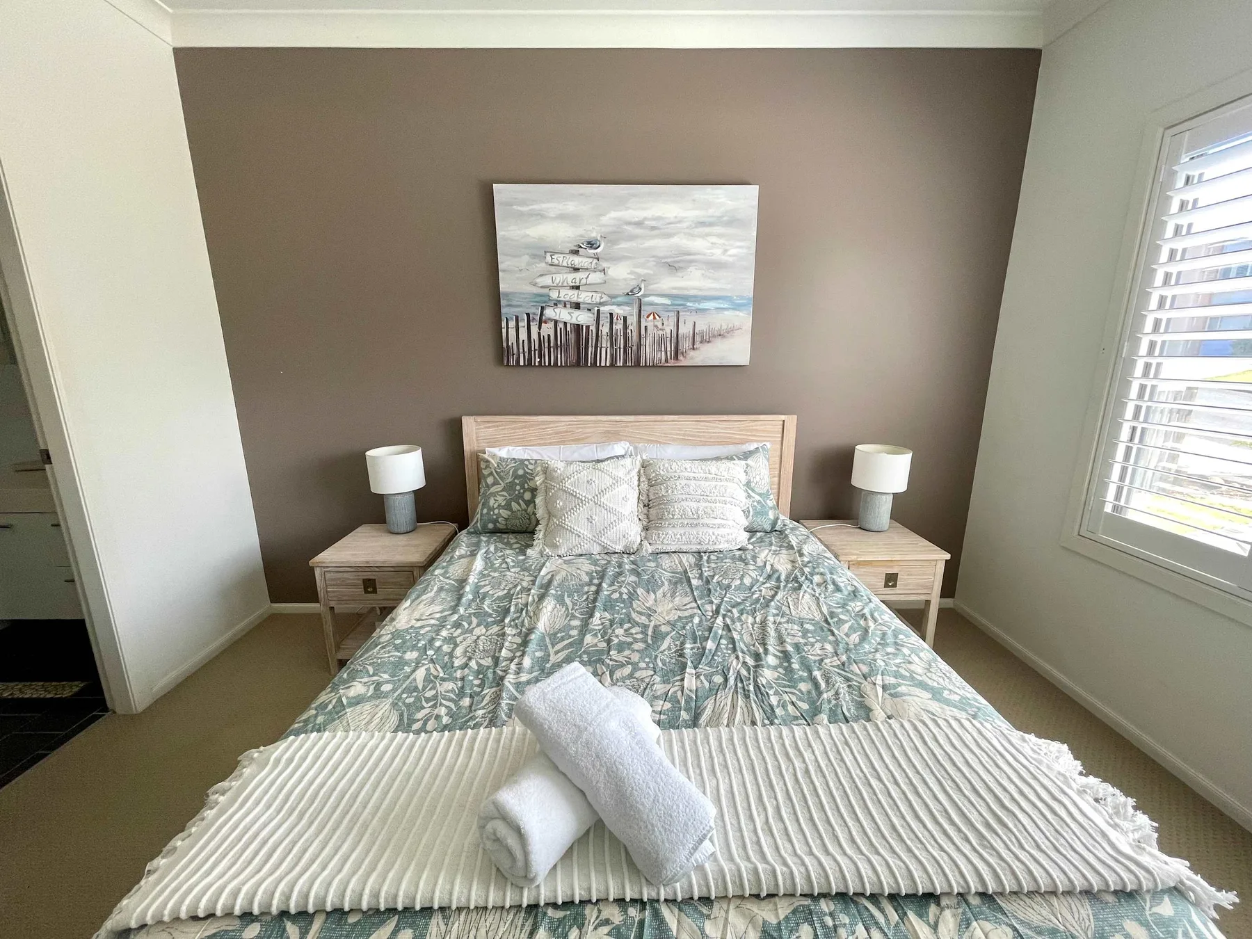 A bedroom with a neatly made bed and coastal artwork above the headboard.