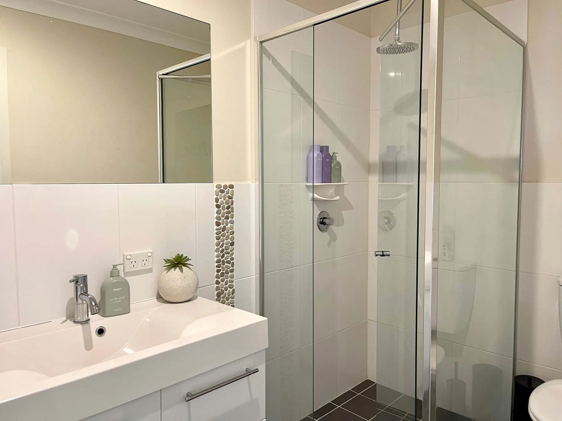 A bathroom with a sink and glass-enclosed shower.