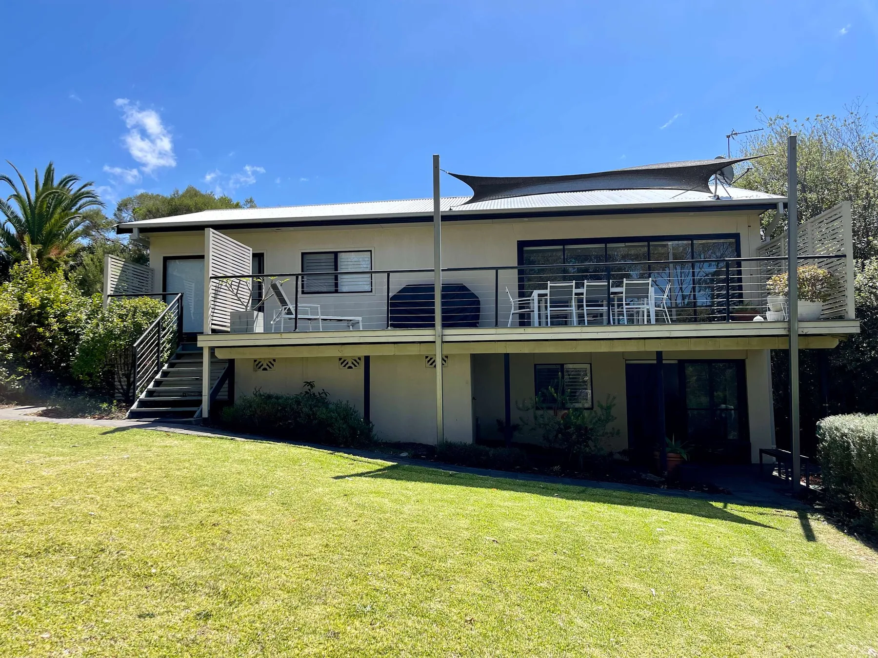 A modern house with a raised deck overlooks a sunny lawn.
