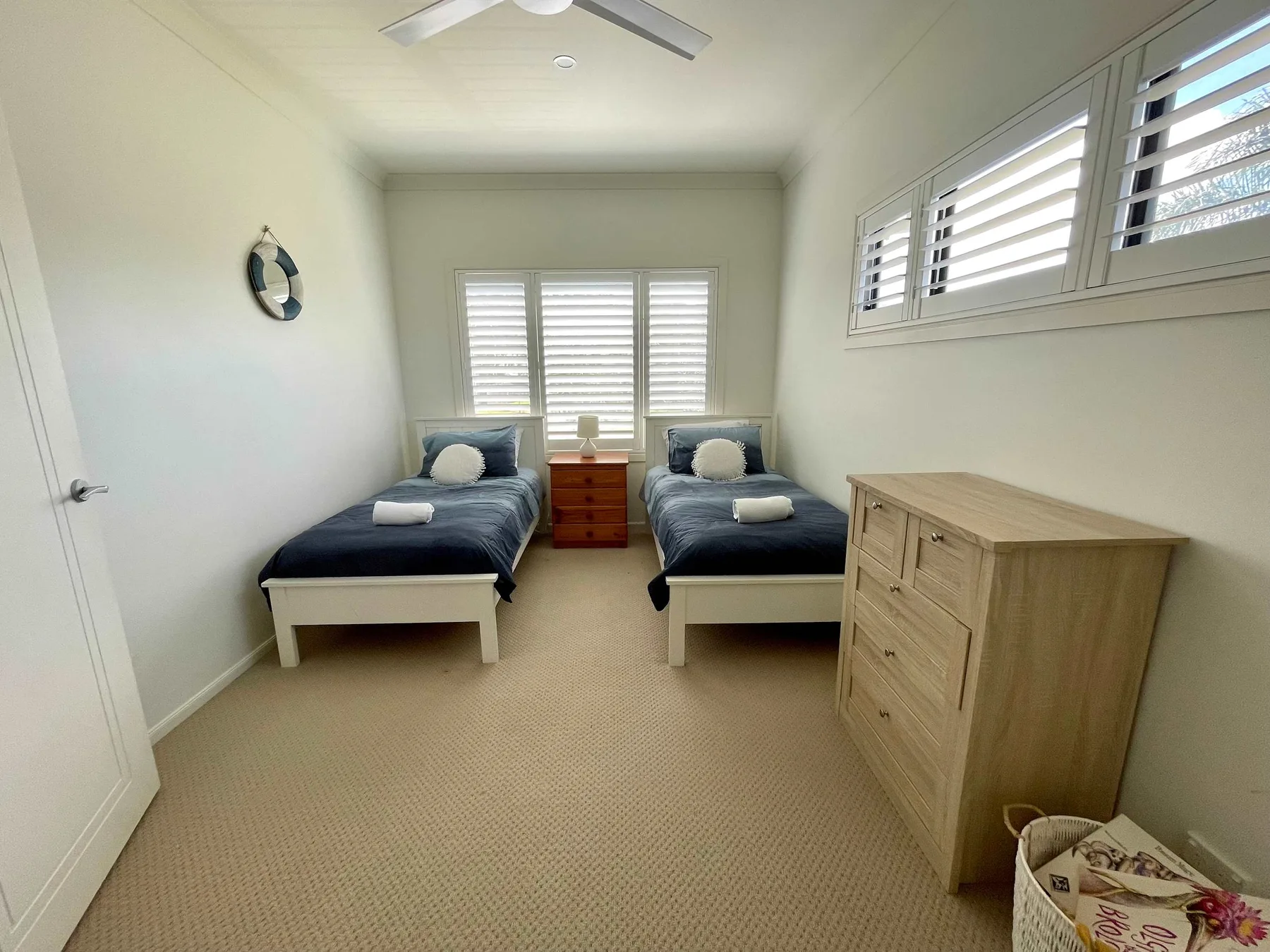 A bright twin bedroom with two beds and a wooden dresser.