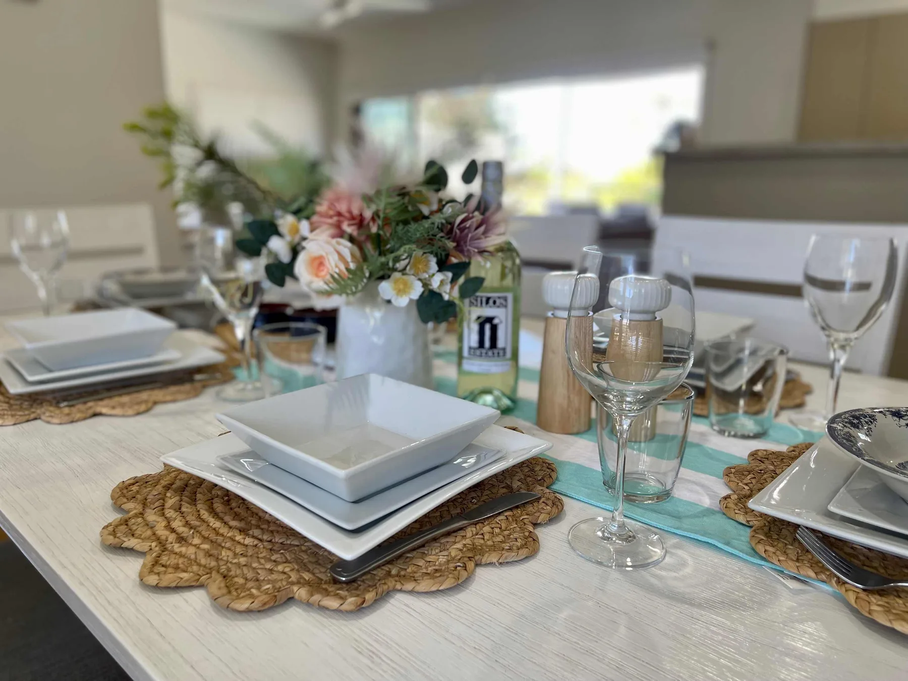 A dining table is set with plates, glassware, and a flower centerpiece.
