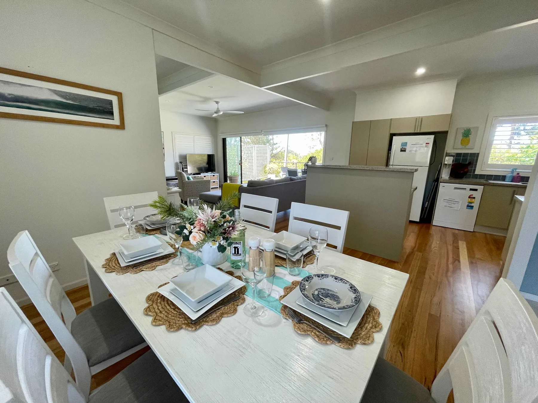 A dining area with a set table opens onto a kitchen and living space.