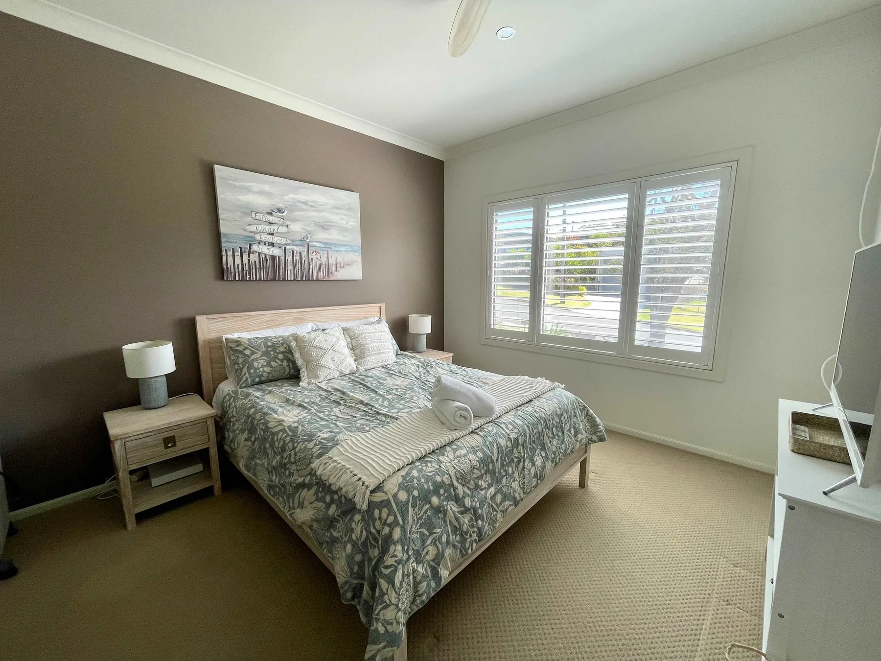 A bedroom with a made bed, bedside tables, and shuttered windows.