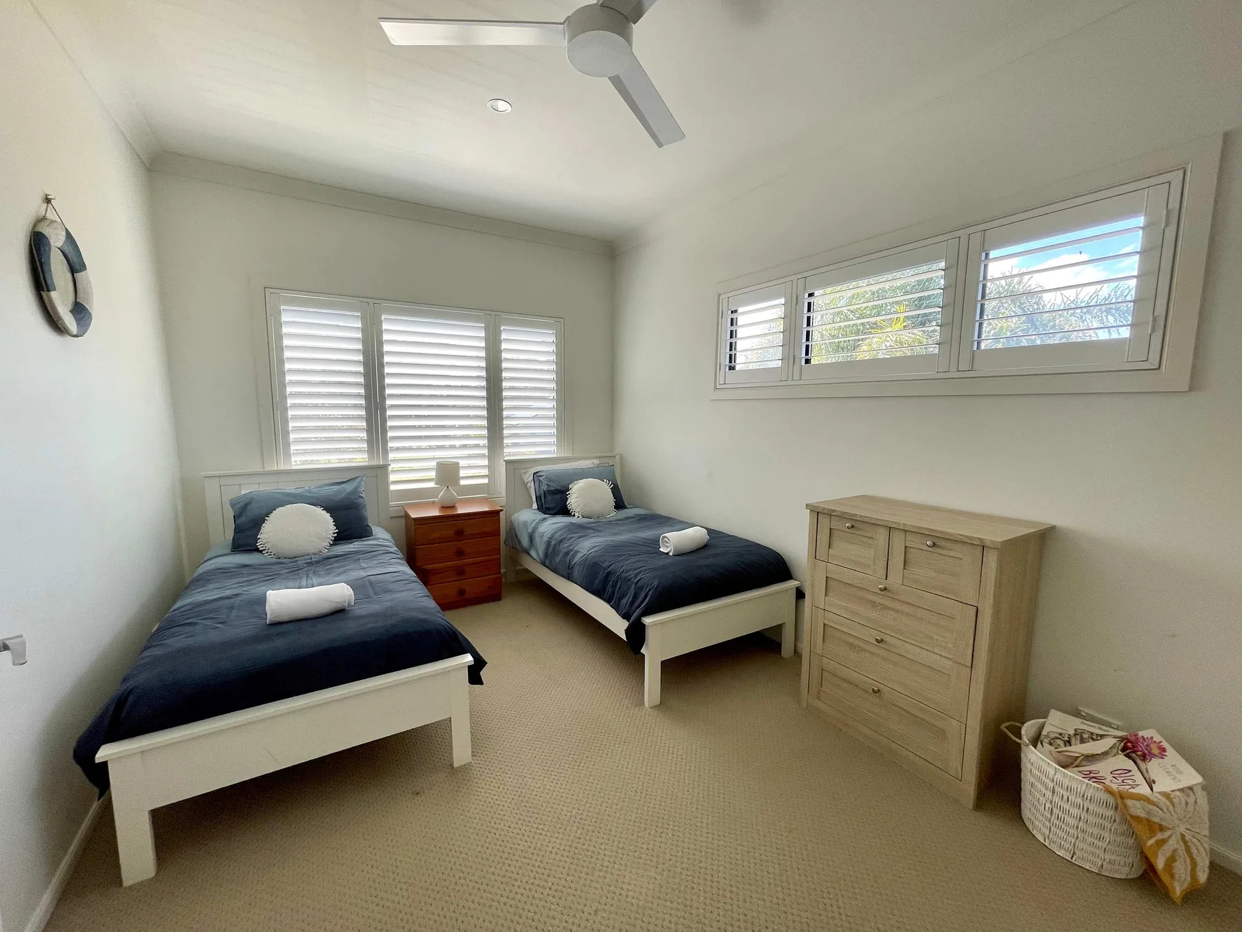 A bright twin bedroom with two beds, shuttered windows, and a wooden dresser.